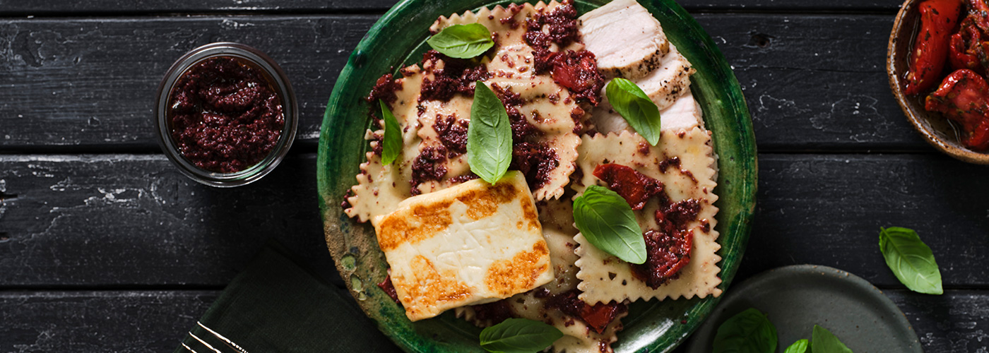 Two bowls of Spinach and Fetta Ravioli with Mediterranean Chicken on a black surface.